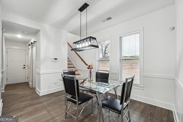 dining space featuring visible vents, dark wood-type flooring, baseboards, stairway, and a barn door