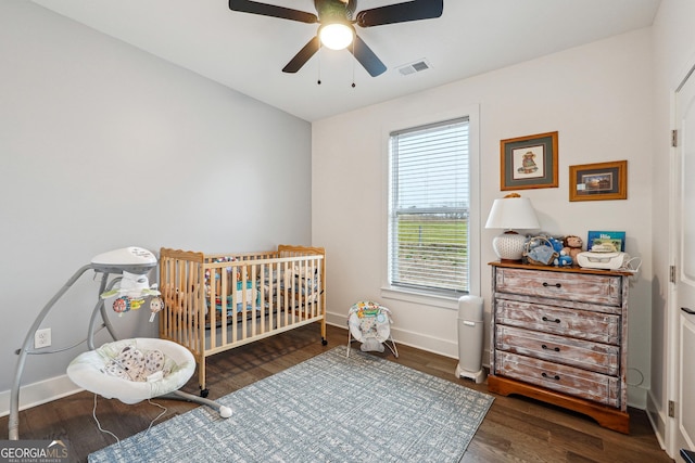 bedroom featuring visible vents, a nursery area, baseboards, and wood finished floors