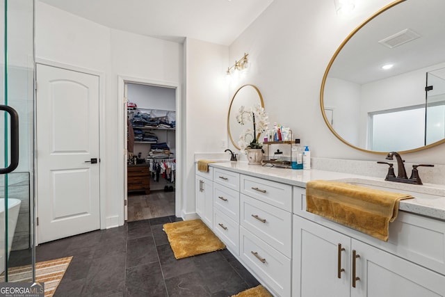 full bath with visible vents, double vanity, a sink, a shower stall, and a spacious closet