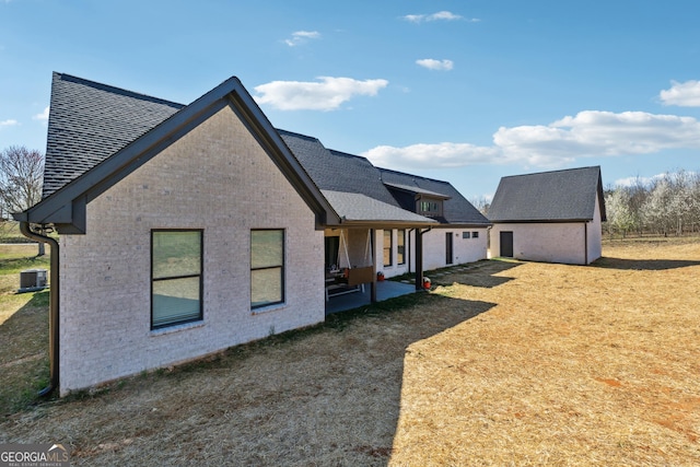 view of side of property with brick siding, an outdoor structure, central AC, and roof with shingles