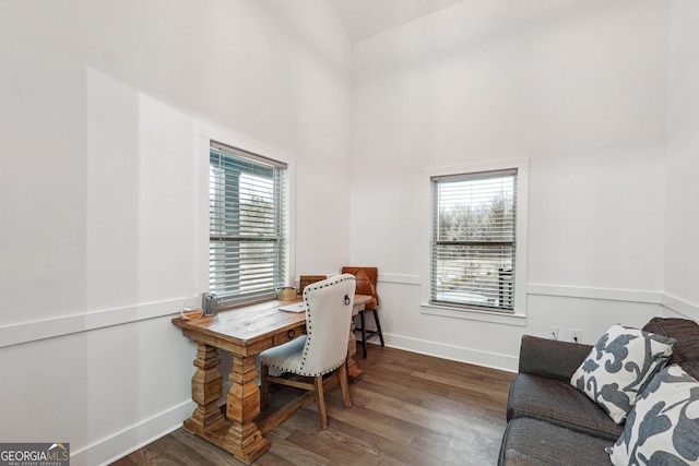 office space featuring a towering ceiling, baseboards, and wood finished floors