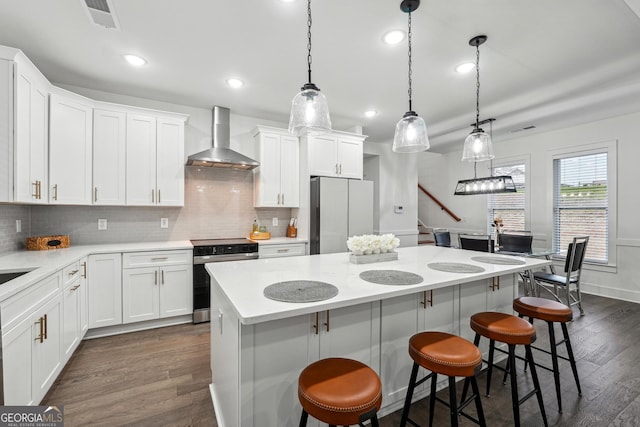 kitchen with a kitchen island, wall chimney range hood, a breakfast bar area, appliances with stainless steel finishes, and dark wood-style flooring