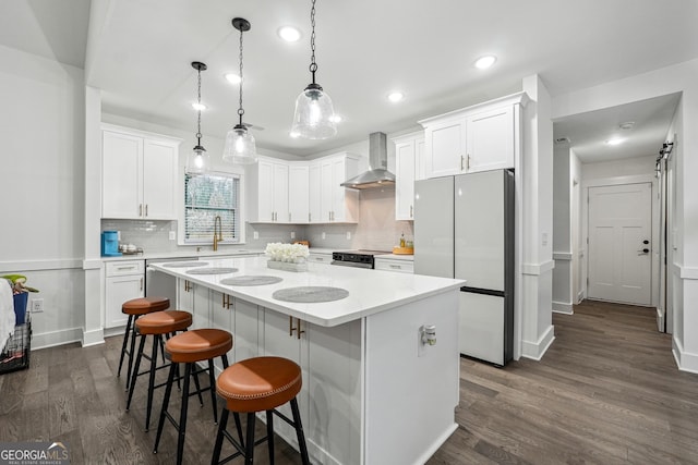 kitchen featuring white cabinets, a kitchen island, freestanding refrigerator, and wall chimney range hood