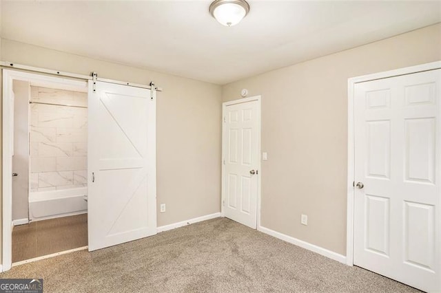 unfurnished bedroom with ensuite bath, a barn door, baseboards, and carpet floors