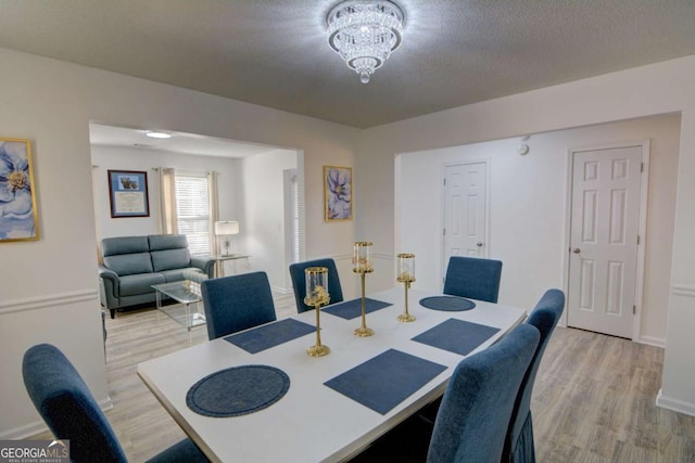 dining room with a chandelier, light wood-style flooring, a textured ceiling, and baseboards