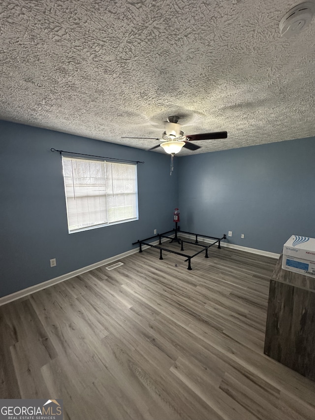 spare room featuring a textured ceiling, baseboards, ceiling fan, and wood finished floors