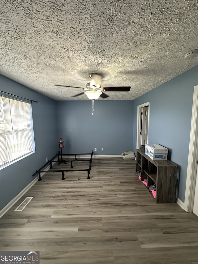 exercise room featuring a ceiling fan, wood finished floors, visible vents, baseboards, and a textured ceiling
