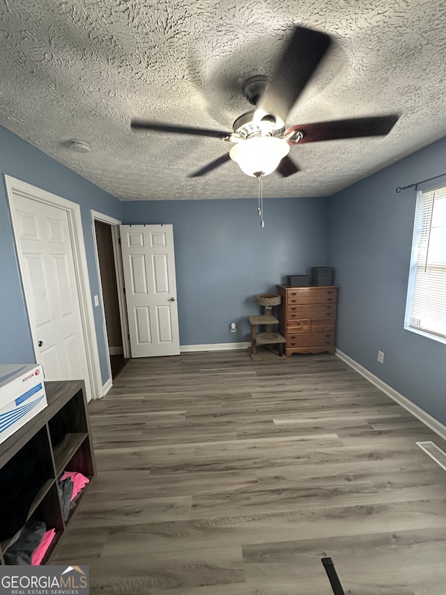 bedroom with ceiling fan, a textured ceiling, baseboards, and wood finished floors