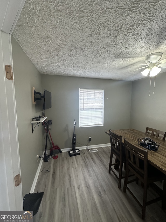 dining space featuring wood finished floors, a ceiling fan, baseboards, and a textured ceiling