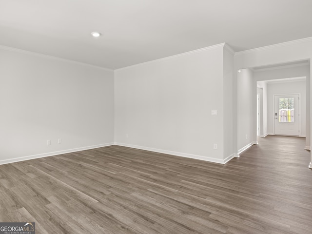 spare room featuring crown molding, baseboards, and wood finished floors