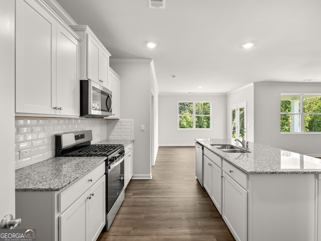 kitchen featuring an island with sink, ornamental molding, a sink, stainless steel appliances, and decorative backsplash