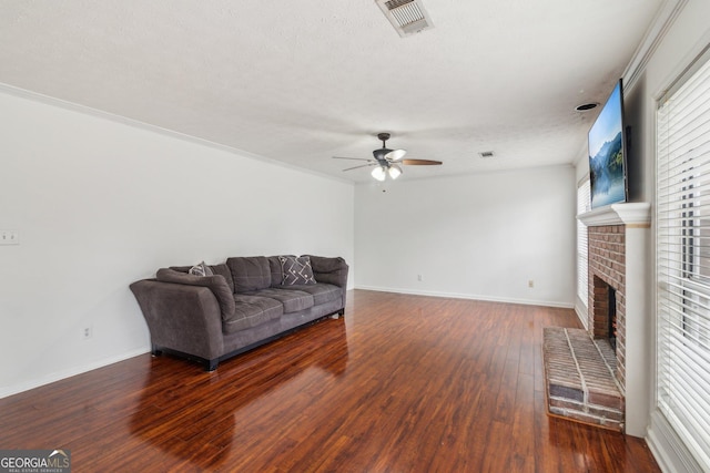 living area featuring visible vents, a ceiling fan, wood-type flooring, baseboards, and a brick fireplace