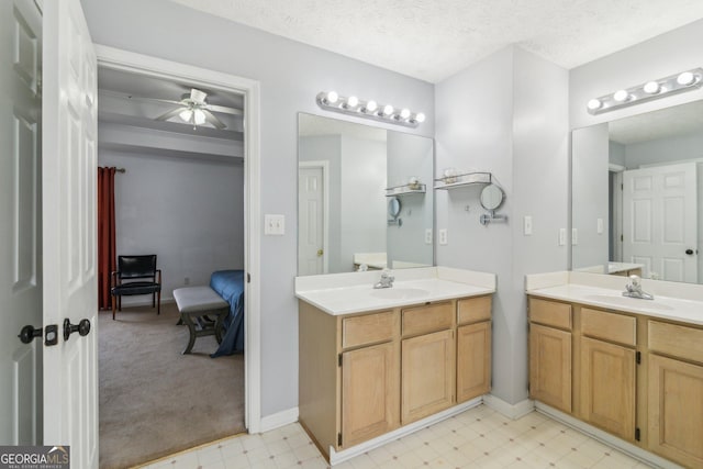 ensuite bathroom featuring a ceiling fan, two vanities, a sink, a textured ceiling, and tile patterned floors