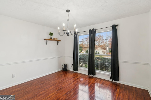 unfurnished dining area with baseboards, wood-type flooring, a textured ceiling, and an inviting chandelier