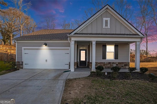 view of front facade featuring driveway, covered porch, a garage, stone siding, and board and batten siding