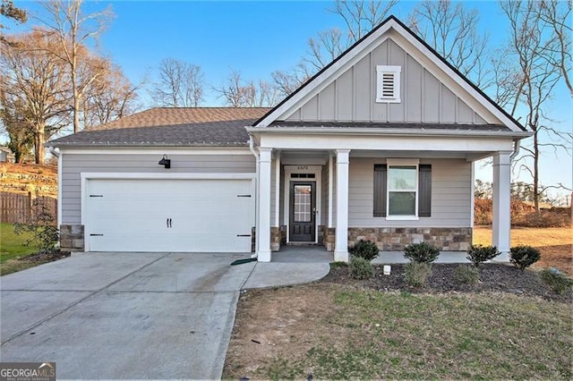 view of front of home with board and batten siding, covered porch, a garage, stone siding, and driveway