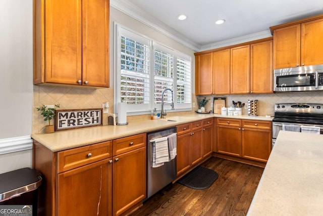 kitchen with a sink, dark wood-style floors, appliances with stainless steel finishes, crown molding, and light countertops