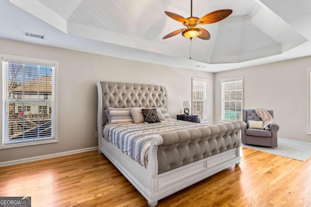 bedroom with wood finished floors, visible vents, baseboards, lofted ceiling, and a raised ceiling