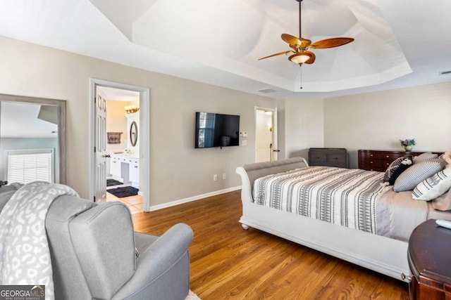 bedroom with visible vents, a ceiling fan, a tray ceiling, wood finished floors, and baseboards