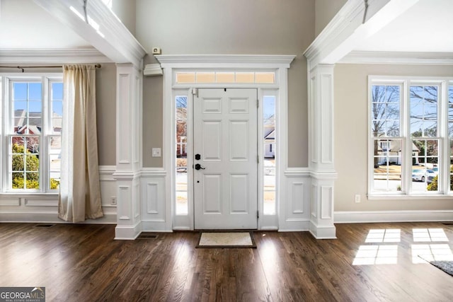 foyer entrance featuring a decorative wall, a healthy amount of sunlight, crown molding, and ornate columns