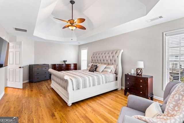 bedroom with visible vents, multiple windows, a tray ceiling, and wood finished floors