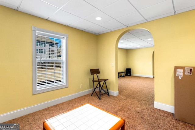 interior space with a paneled ceiling, carpet, arched walkways, and baseboards