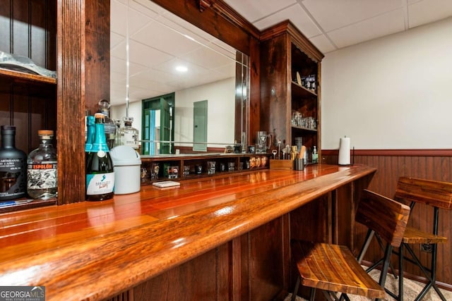 bar with a dry bar, a wainscoted wall, and a drop ceiling