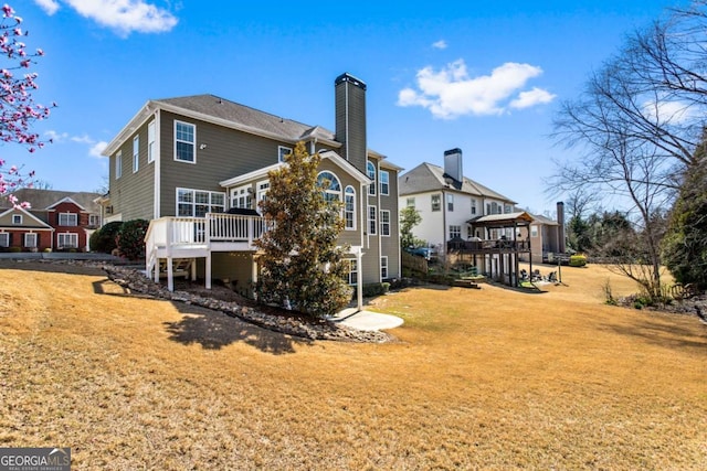 rear view of property featuring a deck, a chimney, and a yard