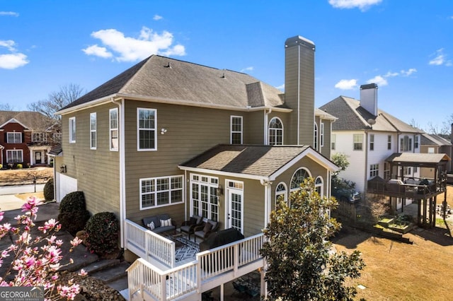 back of property with a shingled roof, an outdoor living space, a deck, and a chimney