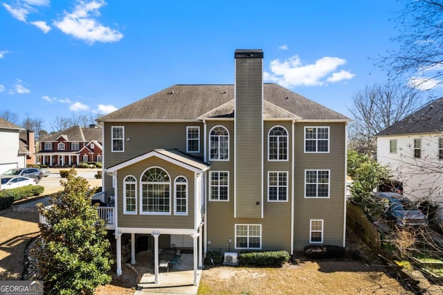 rear view of house featuring a shingled roof, a patio, and a chimney