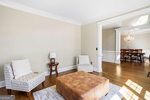 sitting room featuring wood finished floors, a wainscoted wall, decorative columns, crown molding, and a notable chandelier