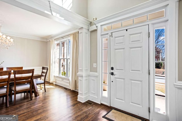 entryway with visible vents, ornamental molding, an inviting chandelier, a decorative wall, and dark wood-style flooring