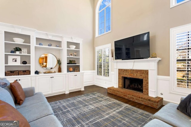 living area featuring dark wood-type flooring, a high ceiling, a fireplace, and wainscoting