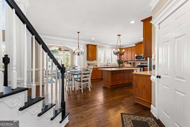 kitchen with a kitchen island, dark wood-style flooring, stainless steel appliances, ceiling fan with notable chandelier, and brown cabinets