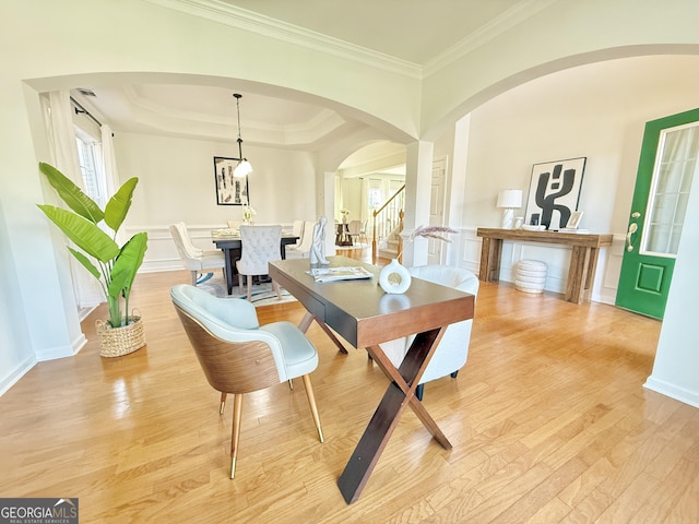 unfurnished dining area with light wood-type flooring, a wainscoted wall, arched walkways, a decorative wall, and a raised ceiling