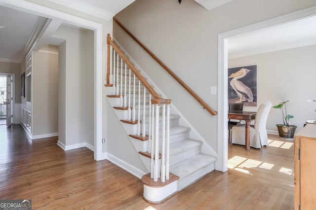 staircase featuring baseboards, wood finished floors, and crown molding