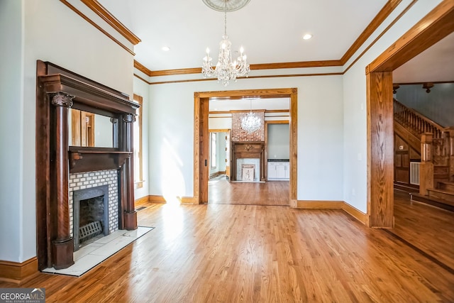 unfurnished living room featuring a notable chandelier, a fireplace, crown molding, and wood finished floors