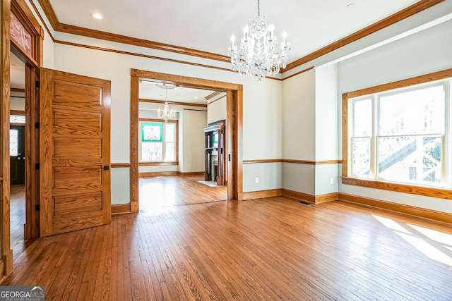 unfurnished room featuring ornamental molding, baseboards, an inviting chandelier, and hardwood / wood-style floors