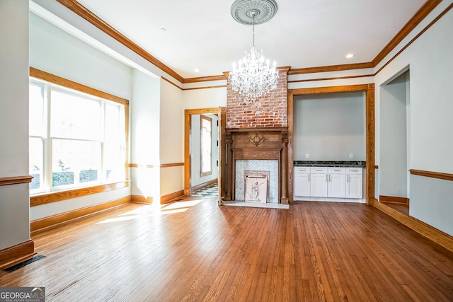 unfurnished living room with visible vents, baseboards, a chandelier, ornamental molding, and hardwood / wood-style flooring