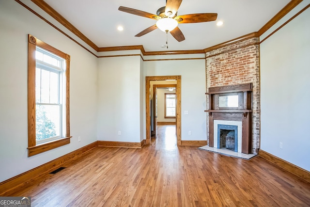 unfurnished living room with visible vents, a brick fireplace, crown molding, baseboards, and wood finished floors