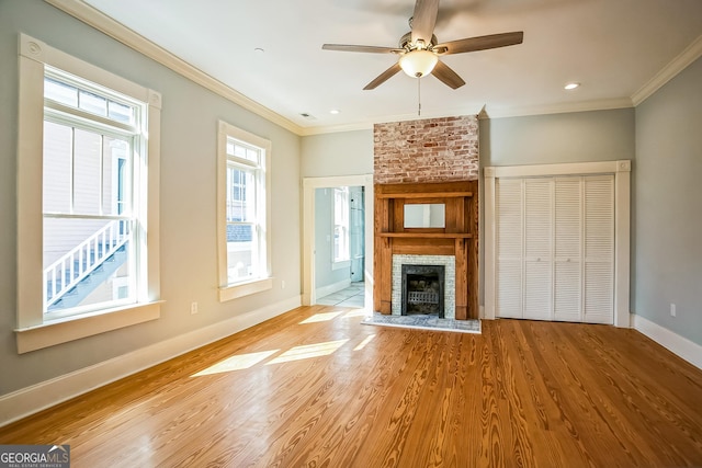 unfurnished living room with a ceiling fan, wood finished floors, crown molding, baseboards, and a brick fireplace