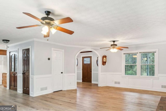 empty room with a textured ceiling, arched walkways, visible vents, and light wood-type flooring