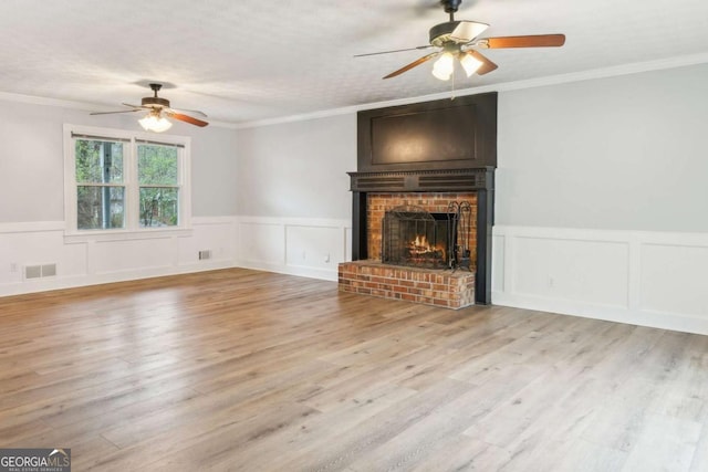 unfurnished living room with visible vents, ceiling fan, ornamental molding, a fireplace, and wood finished floors