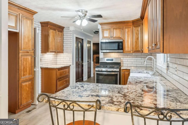 kitchen featuring visible vents, a sink, light stone counters, appliances with stainless steel finishes, and a peninsula