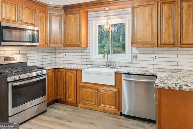 kitchen with brown cabinetry, light wood-type flooring, appliances with stainless steel finishes, and a sink