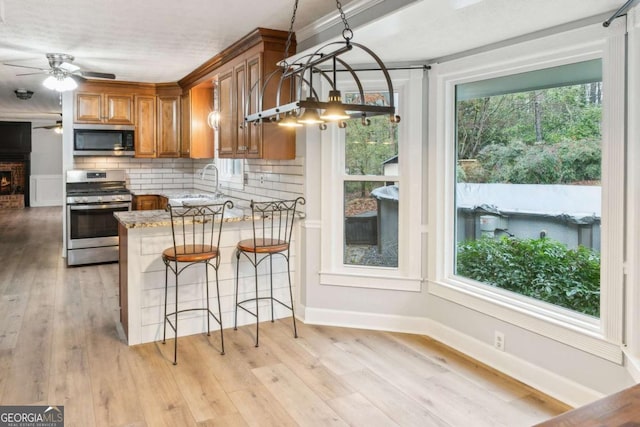 kitchen featuring decorative backsplash, light wood-style flooring, brown cabinets, and appliances with stainless steel finishes