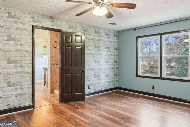 spare room featuring visible vents, a textured ceiling, baseboards, and wood finished floors