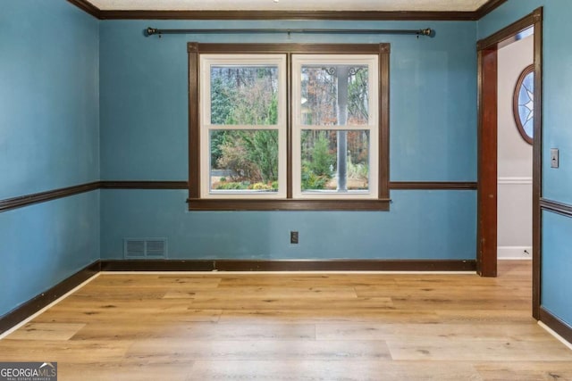 empty room featuring visible vents, crown molding, baseboards, and wood finished floors