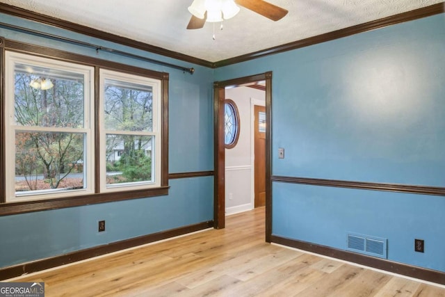 unfurnished room featuring light wood-type flooring, visible vents, ornamental molding, a ceiling fan, and baseboards