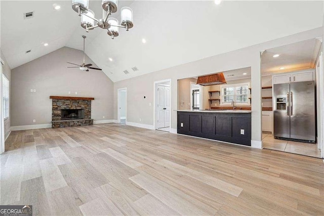 unfurnished living room featuring visible vents, ceiling fan with notable chandelier, light wood-style floors, high vaulted ceiling, and a sink